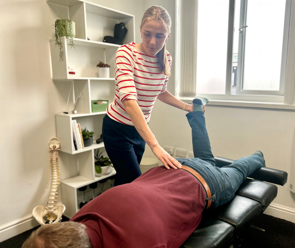 Chiropractor treating patient with low back pain, stretching patient's leg while holding his low back. Taking place in a medical setting of a modern chiropractic clinic